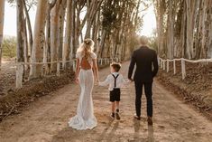 a man and woman holding hands while walking down a dirt road with a young boy