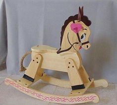 a wooden rocking horse with a pink bow on its head and tail, sitting in front of a gray table cloth