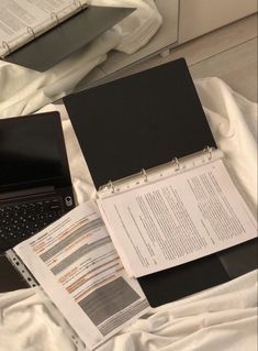 an open laptop computer sitting on top of a bed next to a pile of papers