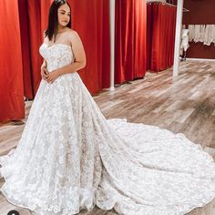 a woman in a white wedding dress posing for the camera with red curtains behind her