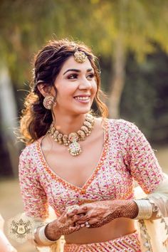 a woman in a pink and white outfit with jewelry on her head, smiling at the camera