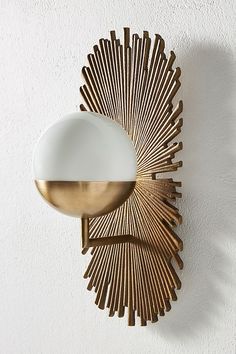 a gold and white wall mounted light on the side of a wall next to a plant