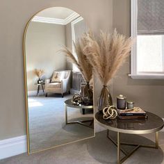 a mirror sitting on top of a table next to a vase filled with dry grass