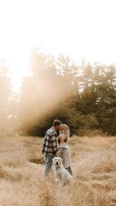 a man and woman standing in tall grass with their dog