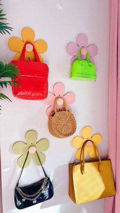 four purses are hanging on the wall next to a plant and flower shaped magnets