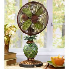 a decorative table fan sitting on top of a wooden table next to a vase filled with flowers