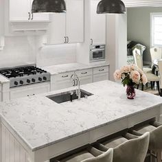 a large kitchen with white cabinets and marble counter tops is pictured in this image, there are four chairs around the island