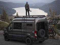 a man standing on top of a van with his bike