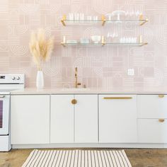 a kitchen with white cabinets and pink wallpaper, gold trimming on the backsplash