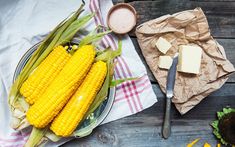 corn on the cob with butter and other ingredients next to it sitting on a wooden table