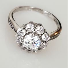 a diamond ring on a white surface with the center stone surrounded by smaller round diamonds