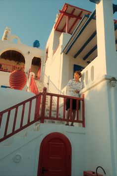 a man standing on top of a balcony next to a red door and white building