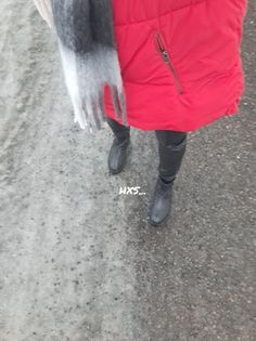 a woman in red coat and black boots walking down the street with an animal on it's arm