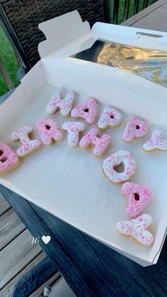 a box filled with pink frosted donuts sitting on top of a wooden table