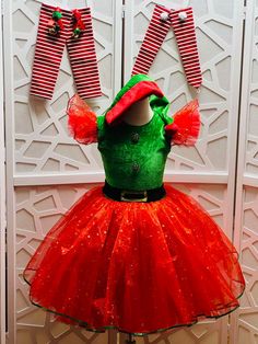 a green and red christmas dress on display in front of a white wall with striped stockings