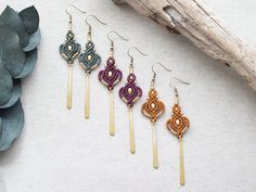 four pairs of beaded earrings sitting on top of a white table next to leaves