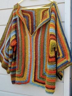 a multicolored crocheted jacket hanging on a white door hanger outside