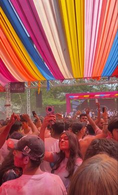 a group of people standing around each other under a colorful canopy at a music festival