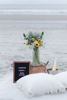 a table set up with flowers, wine glasses and a chalkboard on the beach