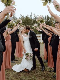 a bride and groom are kissing in front of their wedding party with hands holding flowers