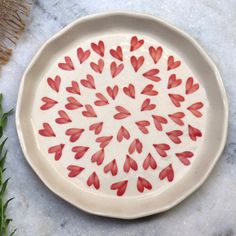 a white plate with red hearts painted on it next to some green leaves and grass