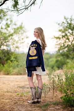 a woman standing in the middle of a field wearing boots and a jacket with an eagle patch on it