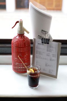 a bottle of alcohol next to a shot glass and menu on a window sill