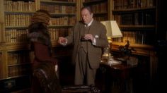 an old man and woman standing in front of bookshelves talking to each other