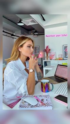 a woman sitting at a desk in front of a laptop computer with her hand on her chin