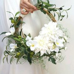 a woman holding a wreath with white flowers and greenery on the inside of it