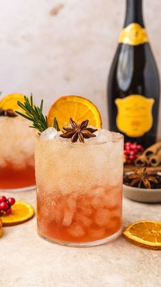 two cocktails with orange slices and rosemary garnish sit next to bottles of champagne