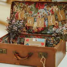 an old suitcase is decorated with flowers and bunting garlands for guests to sign