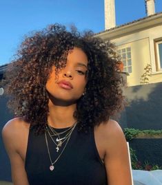 a close up of a person wearing a necklace and a black top with a house in the background