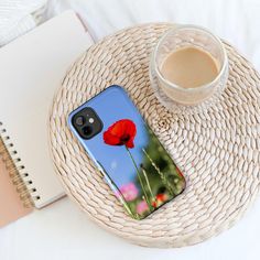 a phone case with a red flower on it next to a cup of coffee and a straw hat