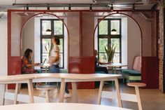 two people are sitting at tables in an office with red and white arches on the walls