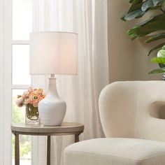 a white vase with flowers on a table next to a chair