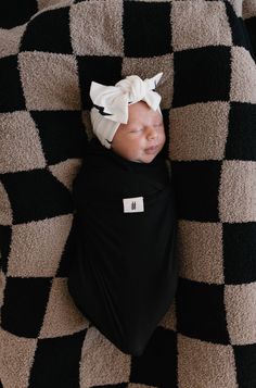 a baby wrapped in a black and white blanket with a bow on it's head