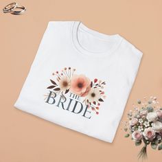 a t - shirt that says the bride with flowers on it next to wedding rings