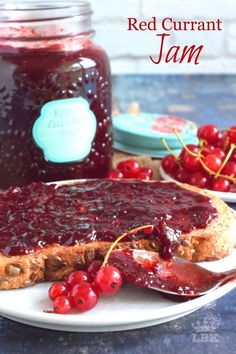 red curran jam is on a plate next to a jar of jam and some cherries