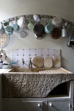 an old kitchen sink with pots and pans hanging on the wall above it's counter