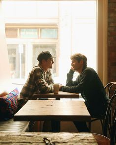 two men sitting at a table in front of a window with the sun shining on them