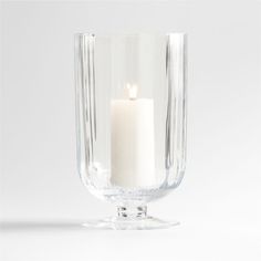 a glass candle holder with a single white candle in it's centerpiece, on a white background