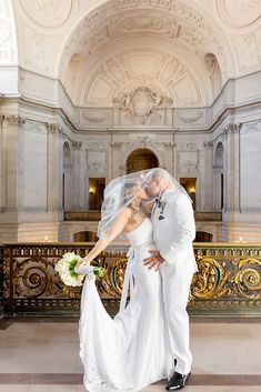 a bride and groom kissing in front of an ornate building with gold railings on either side