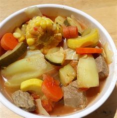 a white bowl filled with meat, vegetables and corn on top of a wooden table