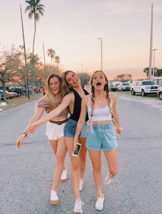 three girls standing in the middle of a parking lot with their arms around each other