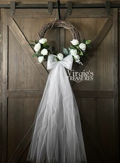 a wedding dress hanging on a barn door with a wreath and flowers in the front