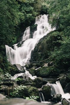 a waterfall in the middle of a forest filled with lots of rocks and greenery