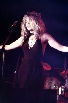 a woman standing in front of a microphone on stage with her arms spread out to the side