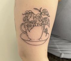 a woman with a tattoo on her arm holding a cup and saucer filled with potted plants