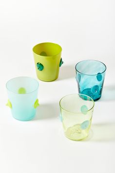 four different colored glass cups sitting on top of a white table next to each other